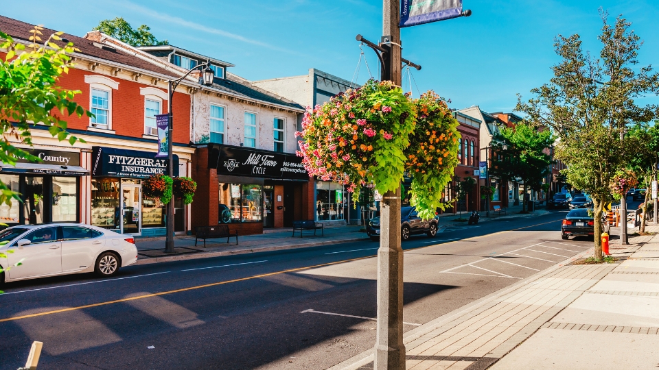 Mill Town Cycle storefront on Main Street in Downtown Milton on a sunny summer day, with colourful hanging flower baskets in the foreground.